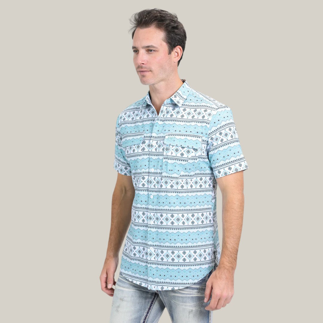 A man stands against a plain grey backdrop, exuding calmness with his hands by his sides while wearing the Mens Performance Western Short Sleeve Aztec Print White Shirt (PGS10627), its light blue color and white/black geometric patterns adding elegance to the scene.