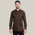 A man with short dark hair wears a Mens Western Modern Fit Spandex Long Sleeve Brown Shirt with Snaps (WPL10487), its subtle pattern highlighted by two chest pockets. It pairs effortlessly with black pants as he stands against a plain gray background.