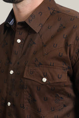 A man wears the Mens Western Modern Fit Spandex Long Sleeve Brown Shirt - WPL10487, featuring snap closures, dark blue horseshoe and horse designs, a chest pocket with a logo, and a comfortable modern fit.