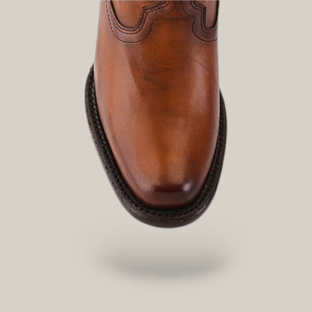 A close-up of a California Tall Shaft Honey boot from the Platinum Collection highlights its brown leather, decorative stitching, and rounded toe with a dark detailed sole against a neutral background.