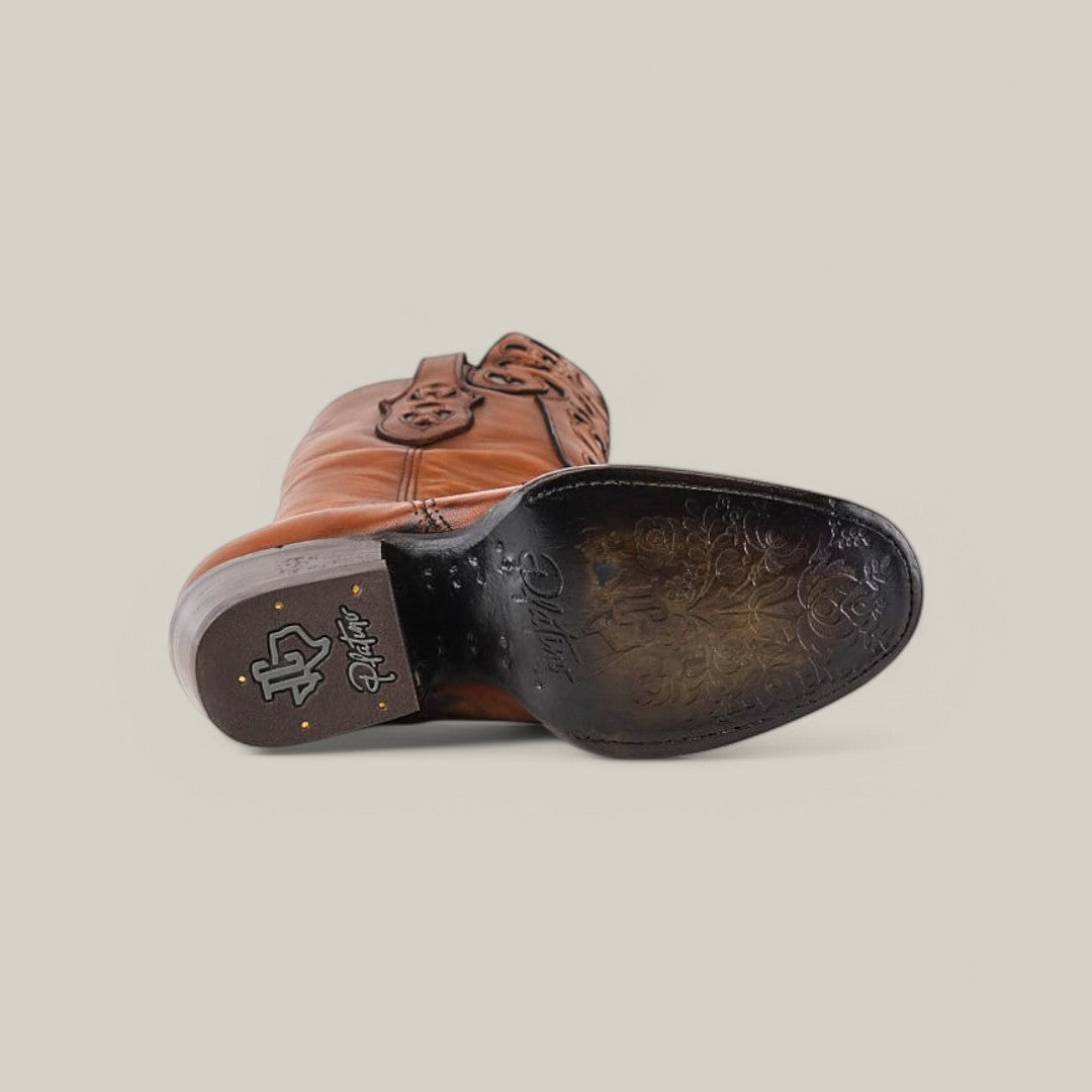 A California Tall Shaft Honey cowboy boot lays on its side, showcasing intricate sole designs. Its polished brown leather surface features branding and ornate patterns, while the round toe pairs beautifully with a plain, light gray background.