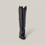 This Francia Rings Tall Shaft Black boot from the Platinum Collection, with a pointed toe and silver chain detailing on a black leather body, sits elegantly against a plain, light grey background. It merges classic style with modern elegance effortlessly.