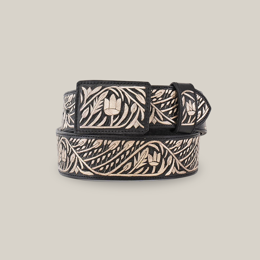 The Artisanal Handmade Silver Belt Flowers Deluxe is a luxurious black belt, intricately designed with silver thread embroidery featuring floral and leafy patterns. Handcrafted and showcased rolled up on a plain white background, it highlights its decorative beauty along the length.