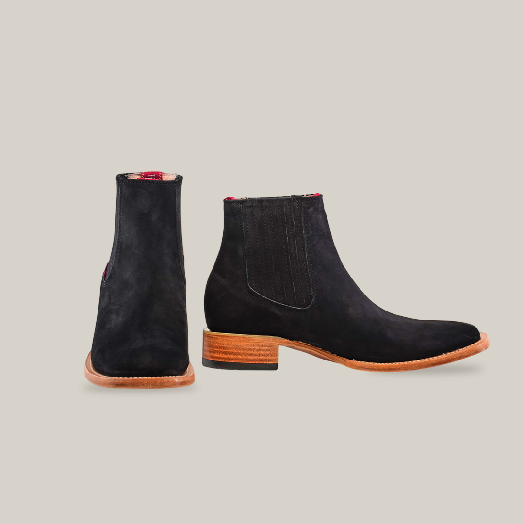 The Prime Suede Black - Square Toe boots feature a black suede exterior with a slight shine, wooden heel, elastic side panels, and rich red interior lining. Showcased on a white background, one boot faces forward while the other is angled to the side.