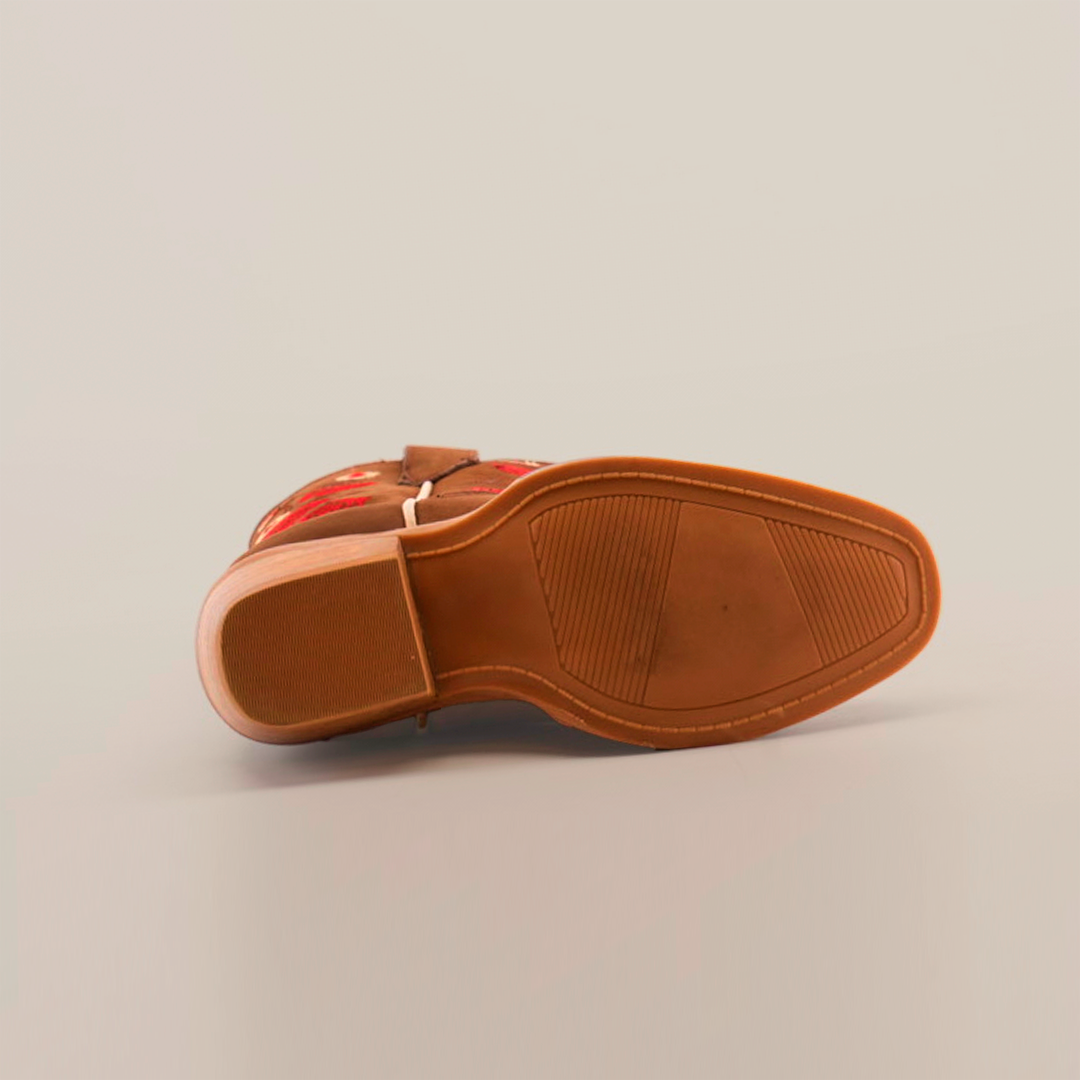 A close-up of a brown leather boot’s sole with a wooden heel, mirroring the handcrafted style of Mia Copper Suede - Snip Toe boots. Red floral embroidery adorns the upper edge, and textured sections on the premium leather sole enhance grip. The background is plain white.