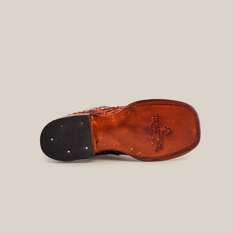 The bottom view of the Exotic Pirarucu Fish Patchwork Cogñac Square Toe shoe showcases a branded logo and text on the sole. The heel includes a rubber section with metallic nail heads. A scuffed appearance adds rugged charm to its worn sole, reminiscent of brown leather square toe boots.