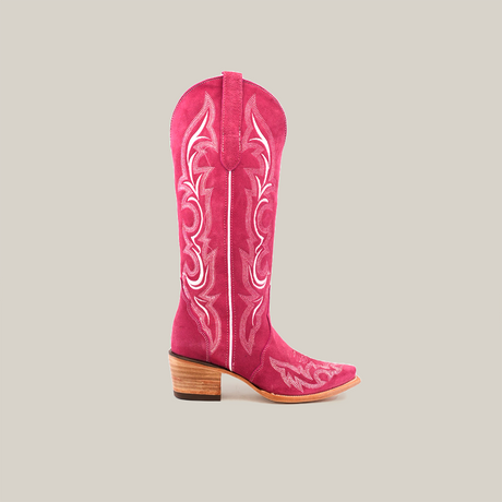 The Amara Pink Suede Tall Shaft boot, featuring a snip toe and decorative white stitching on its vibrant pink surface, is set against a plain white background, highlighting its classic Western style with a wooden heel.