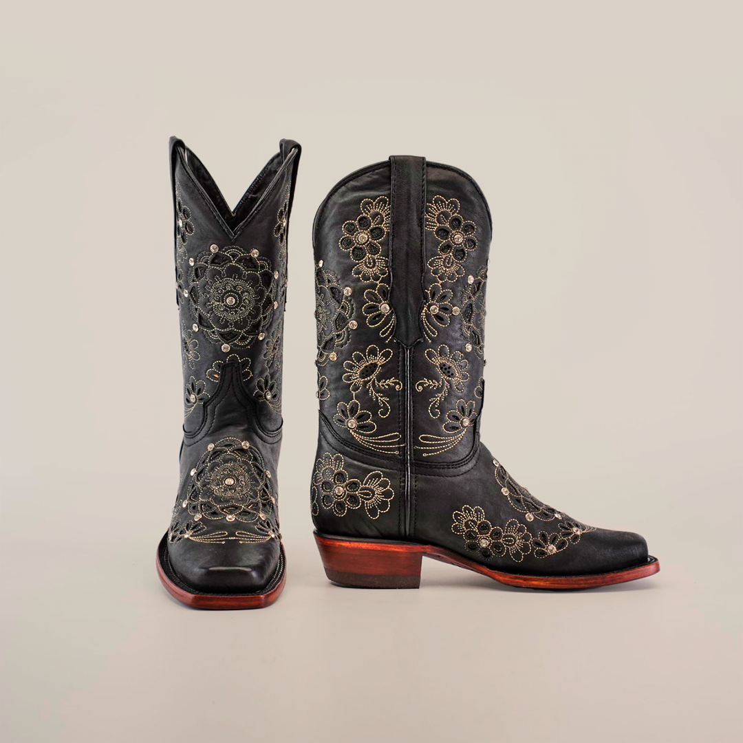 The Mayan Flower Crystals Black boots, featuring a handcrafted short shaft and narrow square toe, are adorned with intricate gold floral embroidery on black leather. These cowboy boots boast a wooden heel and are showcased against a plain white background.