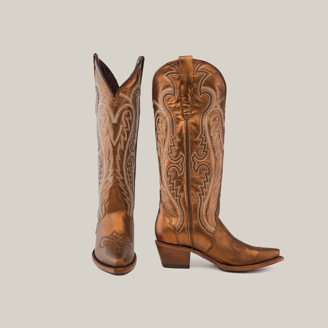 The Nihan Copper - Tall Shaft - Snip Toe boots, featuring intricate shaft stitching and pointed toes, highlight traditional craftsmanship. One boot stands upright while the other tilts slightly, showcasing their handcrafted excellence against a plain light gray background.