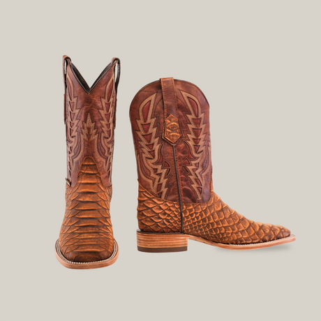 A pair of Jumbo Python Print Cogñac cowboy boots, showcasing a square toe design and decorative stitching, is displayed on a white background. One boot is upright, revealing the side and heel, while the other shows the front.