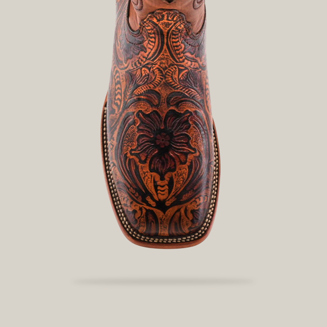 A close-up of the Handtooled Leave Orix - Square Toe cowboy boot highlights its premium cowhide construction with intricate floral patterns, detailed edge stitching, and a polished finish, set against a white background.