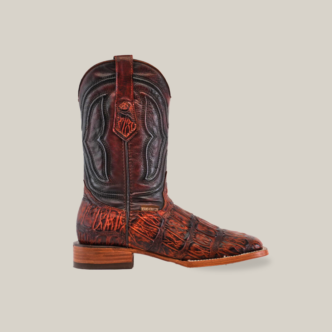 Side view of the handcrafted Gator Print Cogñac - Square Toe boot against a white background, featuring premium cowhide leather, intricate dark stitching, and a detailed pattern. With a wooden heel and square toe, it exudes elegance in its rich brown design.