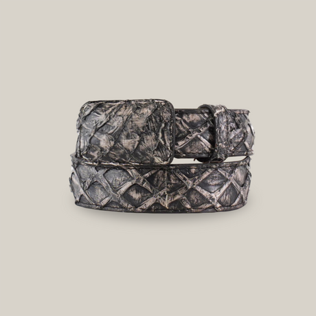 The Exotic Full Quilt Rustic Bone Belt is coiled in a circle, showcasing a diamond pattern with a rectangular buckle. Crafted from Pirarucu fish leather, it has an exotic allure with dark tones and shiny finish resembling metal or leather on a plain white background.