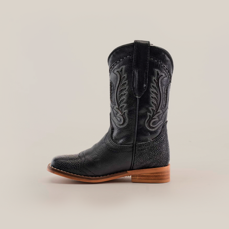 The Stingray Half Cowhide Print Black Rodeo Toe cowboy boot, crafted from cowhide leather with intricate stitching and a textured shaft design, exudes western charm. It boasts a wooden heel and smooth leather sole, standing out boldly against a white background.