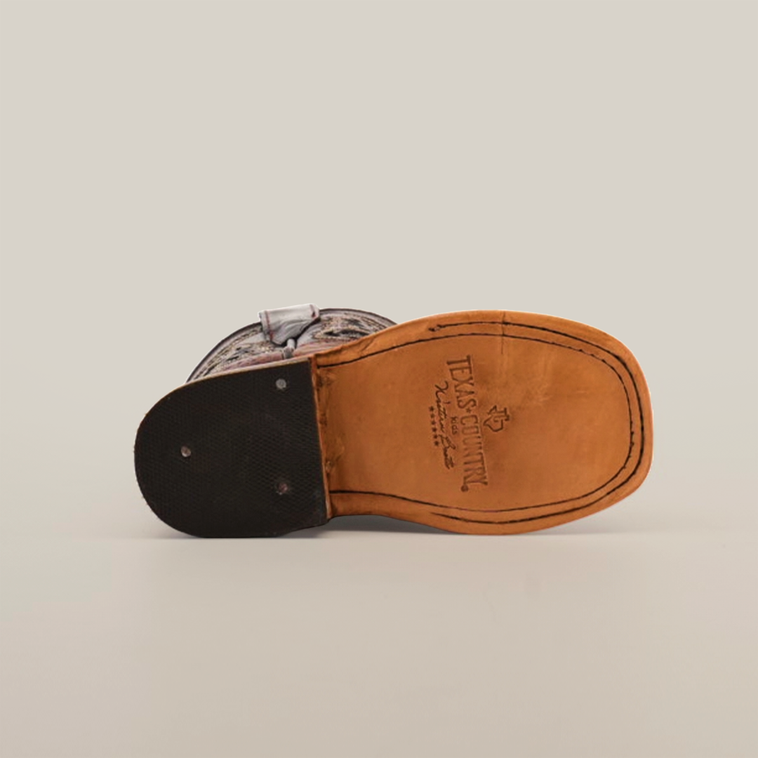 The image features the bottom of a Western-style Caiman Hornback Print Chocolate Square Toe boot with a tan leather sole and black heel. Engraved text and a TEXAS COUNTRY logo adorn the sole, showcasing exquisite craftsmanship against a plain white background.