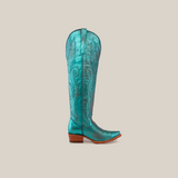 A single turquoise Brittany Rustic Ceramic Tall Shaft Snip Toe Boot displays intricate stitching, patterns, a pointed toe, and a wooden heel. This handcrafted boot features a genuine leather sole on a pristine white background.