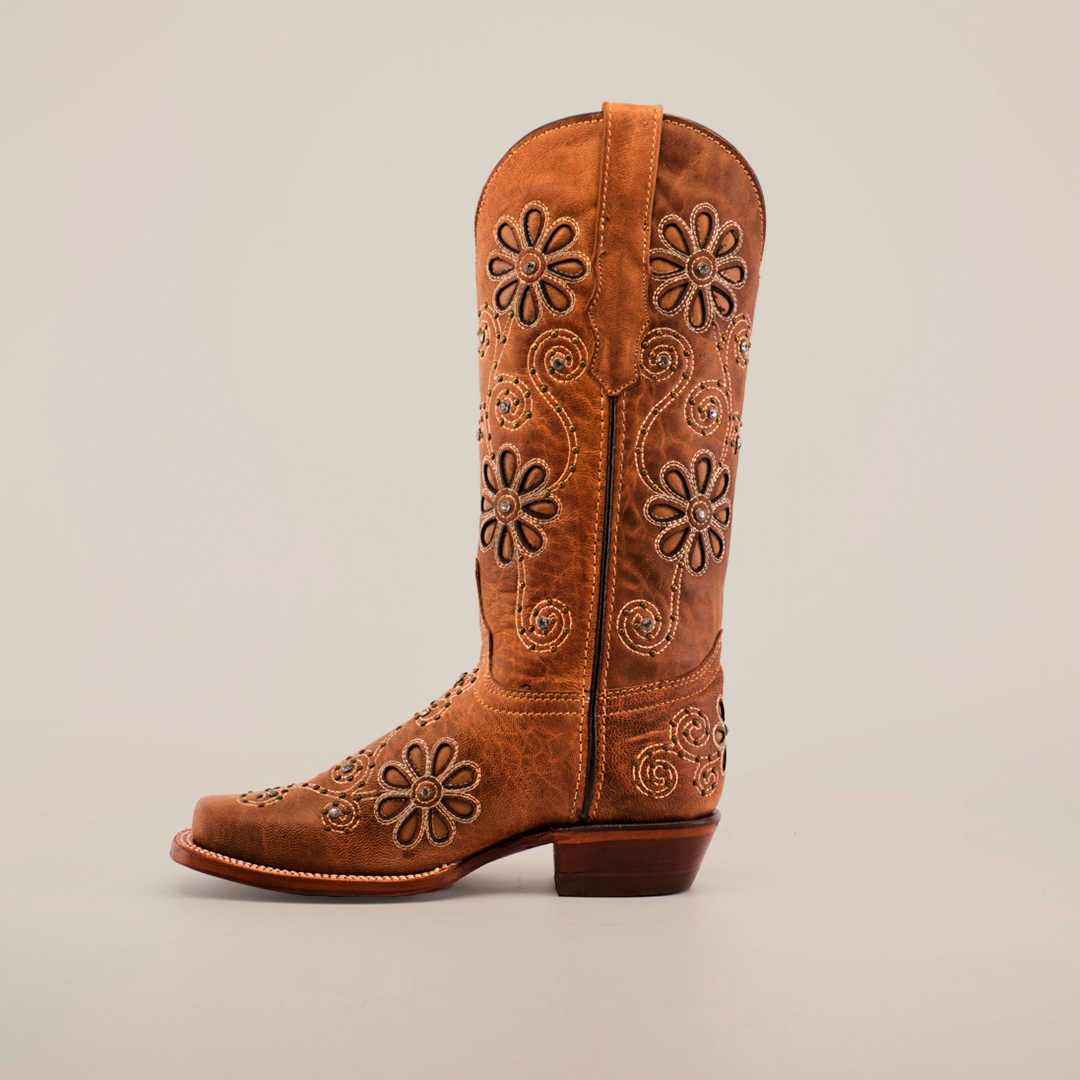 The Napoles Crystals Flowers Fawn boot, featuring intricate floral embroidery with daisies and swirling patterns, is expertly crafted from luxury leather. This handcrafted boot has a narrow square toe, sturdy heel, and convenient pull straps, all highlighted against a plain white background.