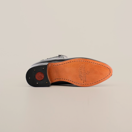 The bottom view of the Napa Black Square Toe shoe reveals its tan sole, detailed stitching, and a rubber nonslip heel featuring a small circular logo. The embossed sole shows brand and size markings. Ideal for fashion-forward wardrobes, its set against a plain white background.