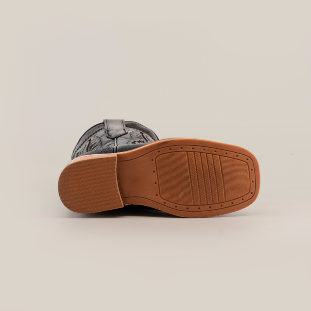 The image displays the bottom view of a Stingray Half Cowhide Print Black Rodeo Toe shoe, featuring a patterned black upper and tan rubber sole. The sole has a rectangular textured area and small circular indentations reminiscent of tiny Stingray boots.