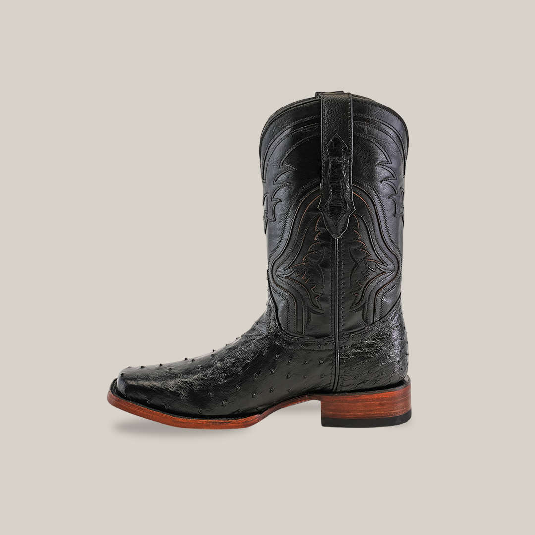 The Exotic Ostrich - Black - Rodeo Toe boot showcases intricate stitching on the shaft, a pointed toe, and a wooden heel. Handcrafted from genuine ostrich leather, it boasts a rugged appearance against a plain background.