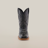 A front view of the Caiman Hornback Print Black Square Toe boot showcases its meticulously handcrafted black leather with ornate stitching, against a plain white backdrop. It features a pointed toe, premium leather with Caiman Hornback print, complemented by a light brown sole and high shaft.