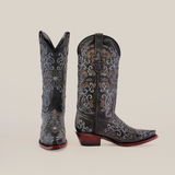 Ornate handcrafted boots with intricate white and brown embroidery on black leather: one boot upright, the other tilted. The Alessandria Black Mid Shaft Snip Toe boots feature pointed toes and wooden heels against a plain white background.