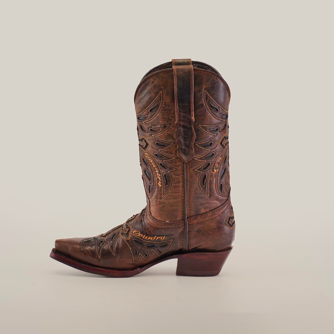 The Texas Cruz Tabaco boot is a single brown womens cowboy boot, made of premium leather with intricate stitching and decorative cutouts. It features a slightly angled heel and snip toe, set against a plain white background.