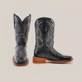 Two Karoo Ostrich Print Black Square Toe cowboy boots with intricate white stitching. Featuring wooden heels, one boot is shown from the front and the other from the side, highlighting their unique texture.