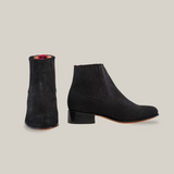 The Prime Suede Black Round Toe boots are displayed, with one upright showing the side profile and round toe design, and the other tilted forward revealing the front. Featuring a slight heel and elastic side panels, they’re perfect for a cowboy-inspired ensemble.