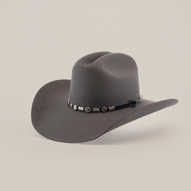 The 6X Dallas Oxford is a wide-brimmed dark gray felt hat with a dented crown and a decorative hatband adorned with circular metal accents, exuding Western sophistication as it rests elegantly on a white surface.