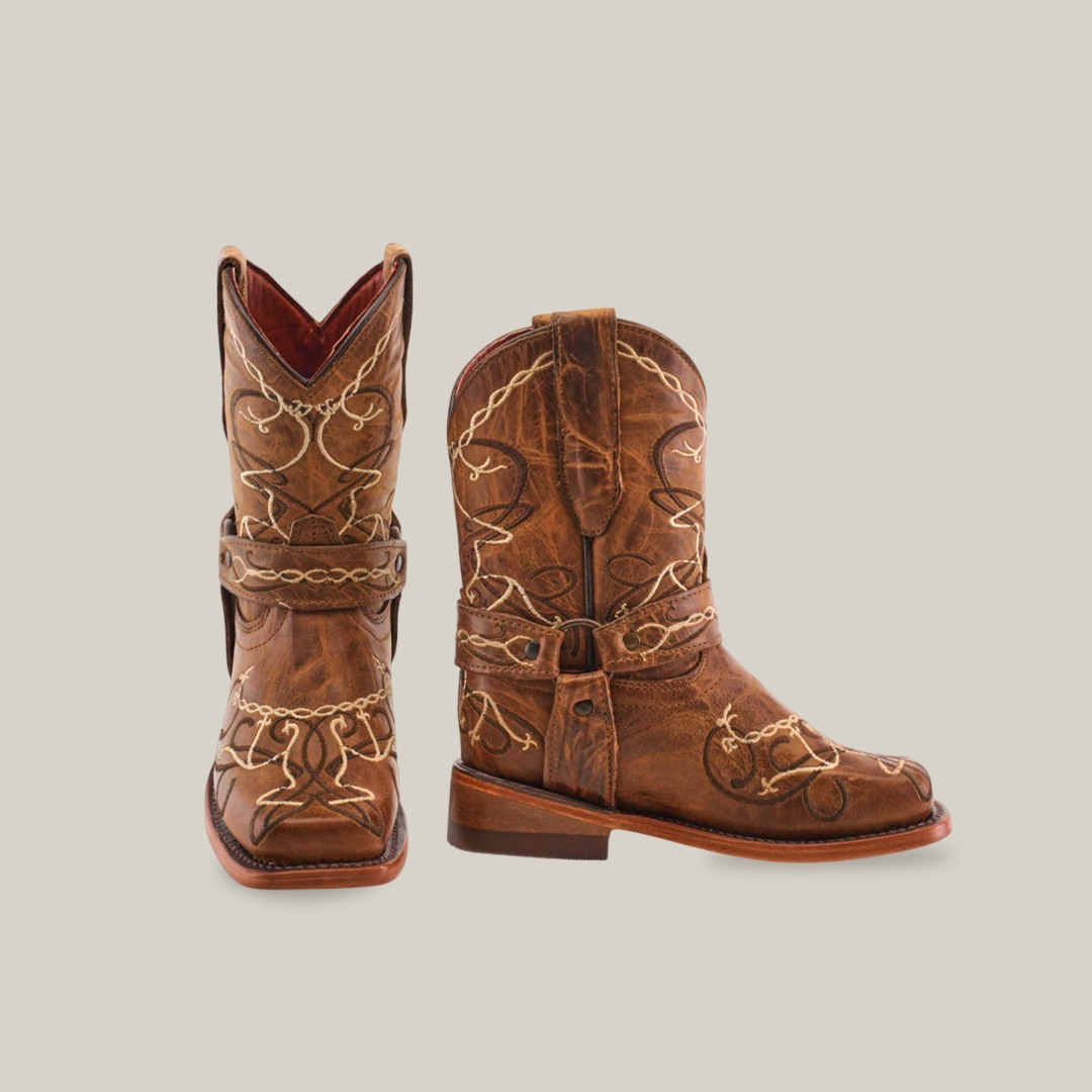 The Graffiti Yellow - Rodeo Toe are genuine leather cowboy boots with decorative stitching and a worn texture. Pictured on a white background, one boot stands upright while the other lies flat, ideal for adventurous young cowgirls.