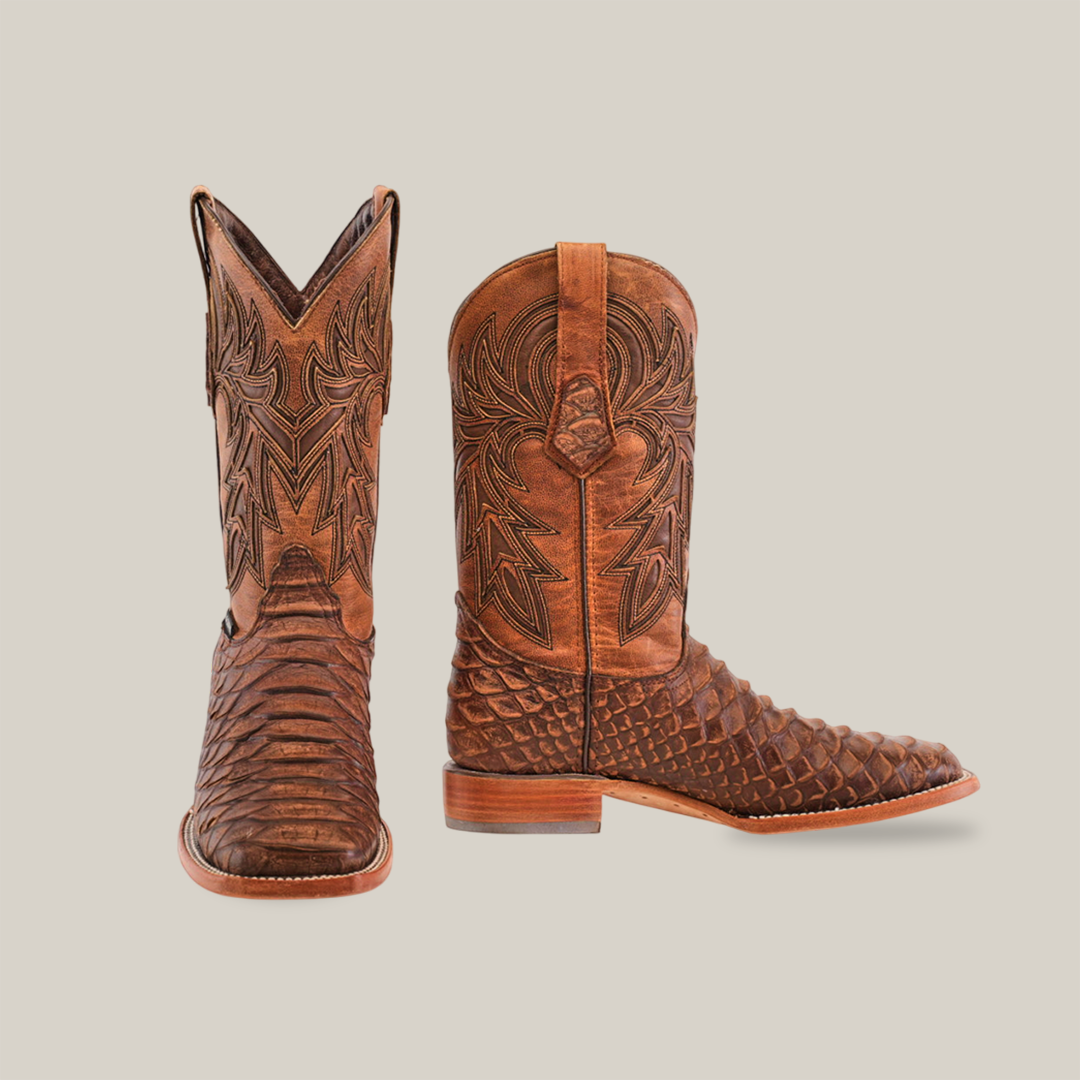 The Jumbo Python Print Rustic Brown boots feature intricate embossed patterns on rustic brown leather, a square toe, and are displayed on a white background with one boot upright and the other on its side, perfect for adding elegance to any western ensemble.