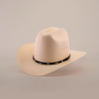 The 500X Dos Carnales Straw Hat, renowned for its quality and durability, boasts a wide brim with a black band at the base. Positioned perfectly on a plain, soft backdrop, this light cream-colored cowboy hat exemplifies style and function.