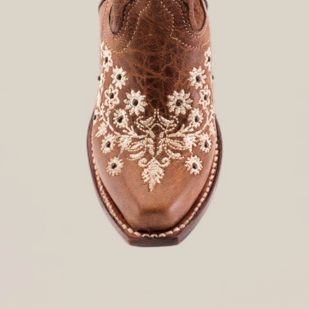 Top view of the Abril Studs Orix Snip Toe boot, showcasing intricate white floral embroidery on brown leather. The detailed stitching adds texture and contrast, while the childrens sole design is visible around the edges.