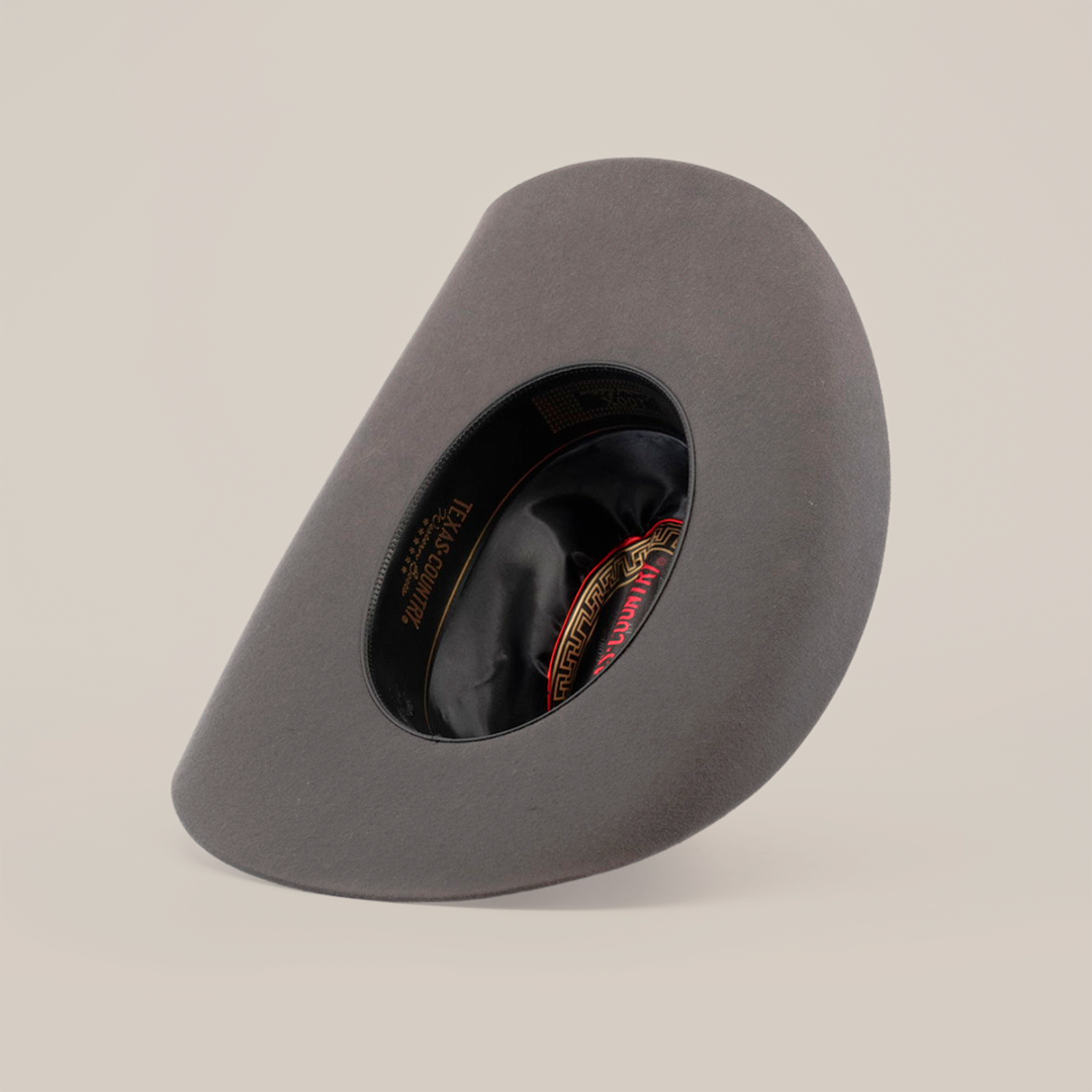 The 6X Dallas Oxford, a gray felt hat that exudes Western sophistication, is shown upside down to reveal its black and red lined interior with a label. It features a smooth brim and structured shape, all set against a plain white background.