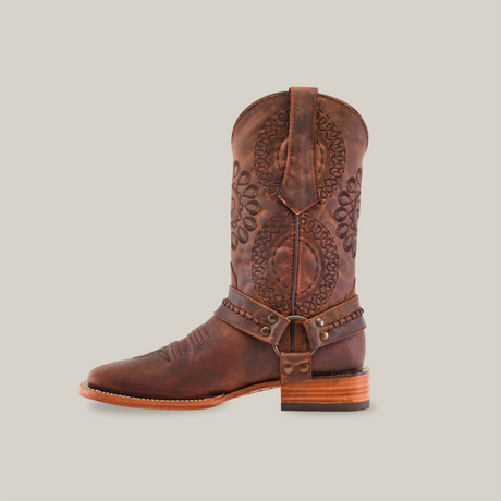 A single handcrafted boot in Matte Brown Country Stitch - Square Toe is presented from the side against a white background, featuring ornate patterns on premium cowhide, a distinctive wooden heel, and decorative elements around the ankle.