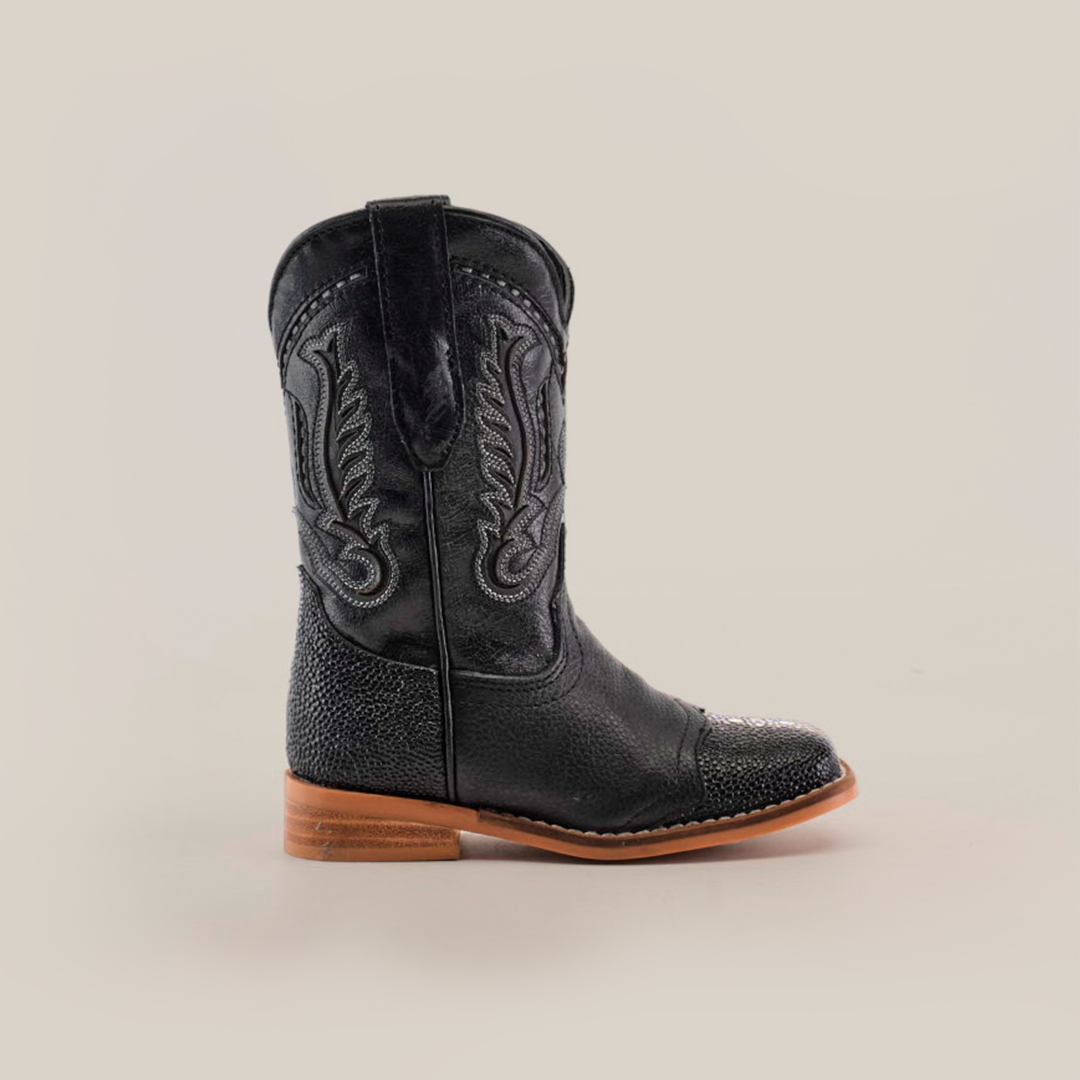 The Stingray Half Cowhide Print Black Rodeo Toe boot showcases intricate Western stitching, a textured cowhide leather lower, and a wooden sole with a low heel, all captured from the side against a plain white background.