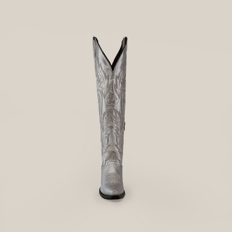 A handcrafted Brittany Silver- Tall Shaft - Snip Toe boot is highlighted against a plain gray background, showcasing premium leather with intricate stitching, a pointed toe, and a high shaft adorned with decorative patterns.