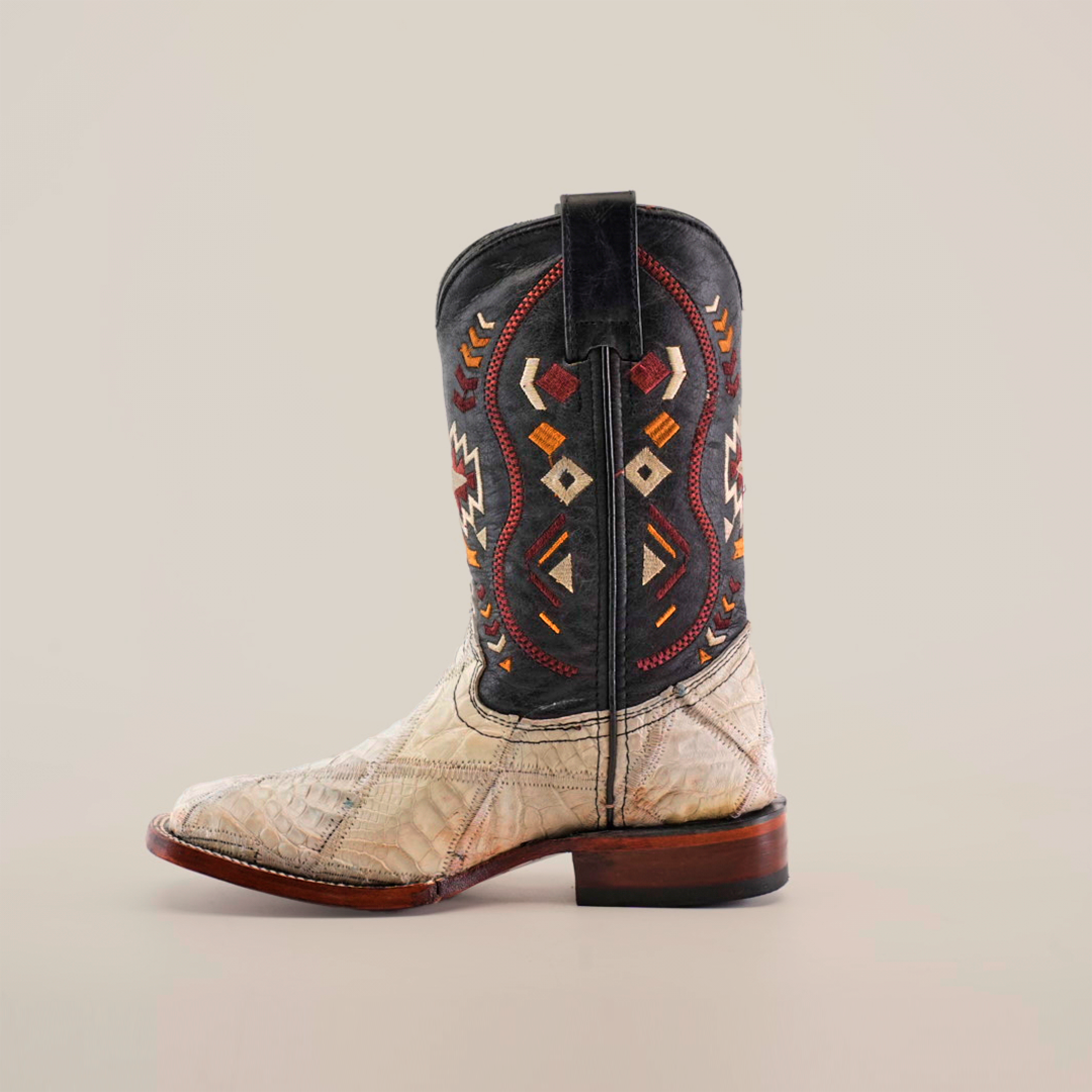 The Exotic American Alligator Patchwork Bone Square Toe boot features a beige alligator-textured foot and a black shaft with colorful geometric patterns. Its square toe design and wooden heel create a classic western style against a plain white background.