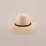 The 1000X Chihuahua Straw Hat, beige with a wide brim and accented by a black band featuring small oval conchos, stands out against a white background, offering a bold fashion statement for those seeking style and durability.