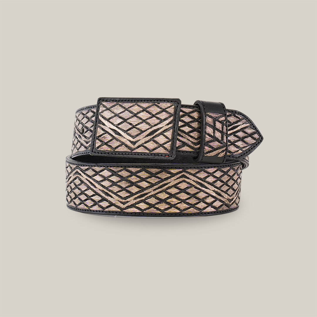 The Artisanal Handmade Silver Belt Rombos showcases a geometric pattern of intersecting diagonal metallic lines with silver thread embroidery. It features a rectangular buckle, black edge, and its design is contrasted beautifully against a plain white background.