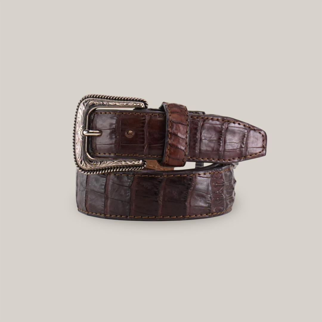 The Exotic Full Quilt Caiman - Texas Buckle - Brown Belt, with its luxurious crocodile leather and silver decorative buckle, exudes Western elegance. Its textured pattern enhances its refined appeal, coiled neatly on a plain white background.