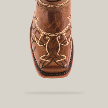 Close-up of a genuine leather cowboy boot, ideal for young cowgirls, featuring intricate white and dark brown embroidery with loops and curves on the toe. This striking boot boasts a square toe design reminiscent of the Graffiti Yellow - Rodeo Toe boots.