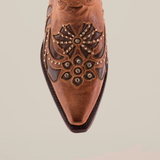 Close-up of the toe of a handcrafted brown leather Cotulla Tabaco Crystals boot, featuring intricate floral embroidery and metal studs. This design marries light and dark brown tones against a white background, embodying Western sophistication.