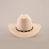 The 1000X Dos Carnales Straw Hat, an exceptional beige cowboy hat with a black band and decorative white oval accents, is displayed against a plain white background.