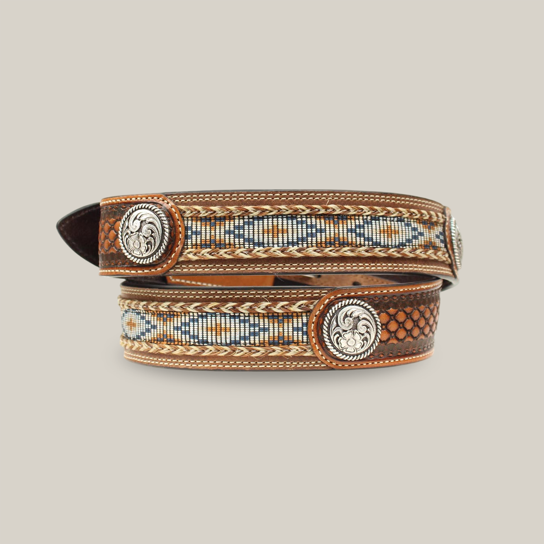 The Ariat Western Mens Belt, model A1013248, features a stylish brown leather basketweave with floral silver conchos. Its intricate beadwork in blue, white, and tan geometric patterns showcases rugged elegance and reflects Western heritage. Coiled to highlight its design.