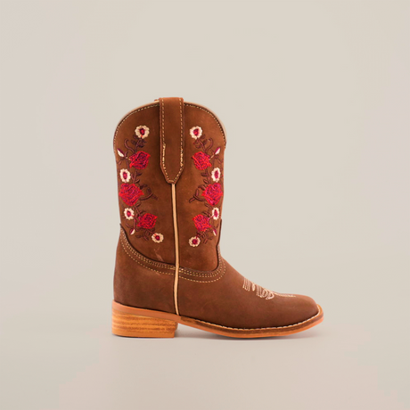 The Mia Copper Suede - Square Toe cowboy boot, with premium brown leather, a wooden sole, and red rose and white flower embroidery, is showcased in profile against a plain white background.