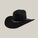 Experience Western sophistication with the 6X Dallas Black cowboy hat. Crafted from Dallas felt, it features a wide brim and creased crown adorned with a black band featuring metallic details, presenting timeless elegance against a crisp white background.