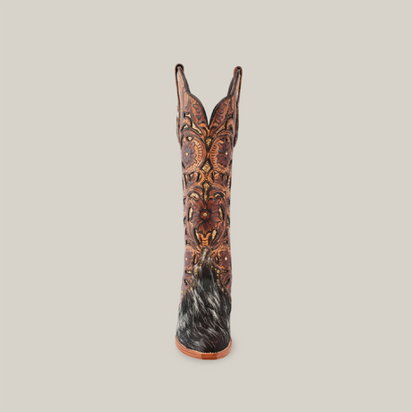 The Handtooled Cowhide Pinto boot features a tall shaft and snip toe, crafted from premium cowhide with ornate floral patterns and dark, textured heel detailing. Its rich reddish-brown color is strikingly set against a plain white background.