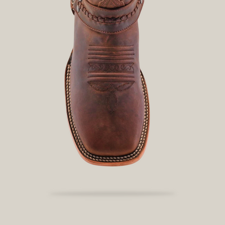 A detailed view of a Matte Brown Country Stitch - Square Toe boot, showcasing its intricate patterns on the toe and upper, decorative embossing, and premium cowhide craftsmanship against a plain, light background.